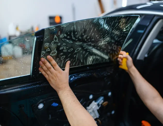 An installer's hands setting tint film on a car door window